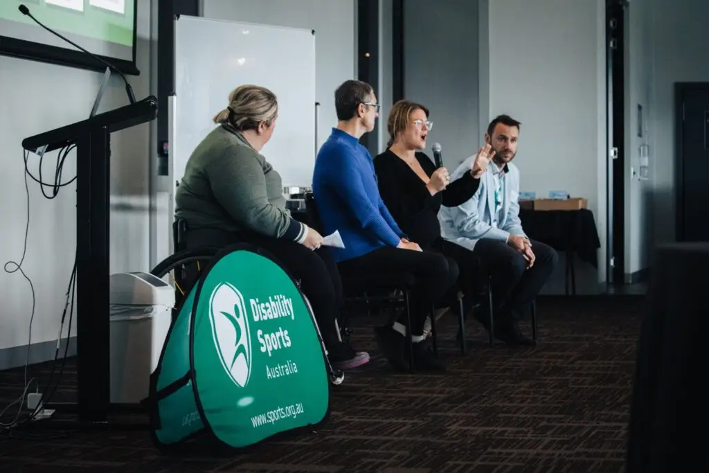 Four people sitting at the front of a room in a panel discussion, with a Disability Sports Australia sign visible.