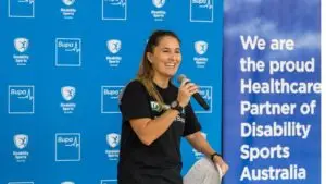 Presenter standing in front of a blue backdrop with Disability Sports Australia and Australian Sports Commission logos, with text reading: “We are the proud National Health Partner of Disability Sports Australia.”